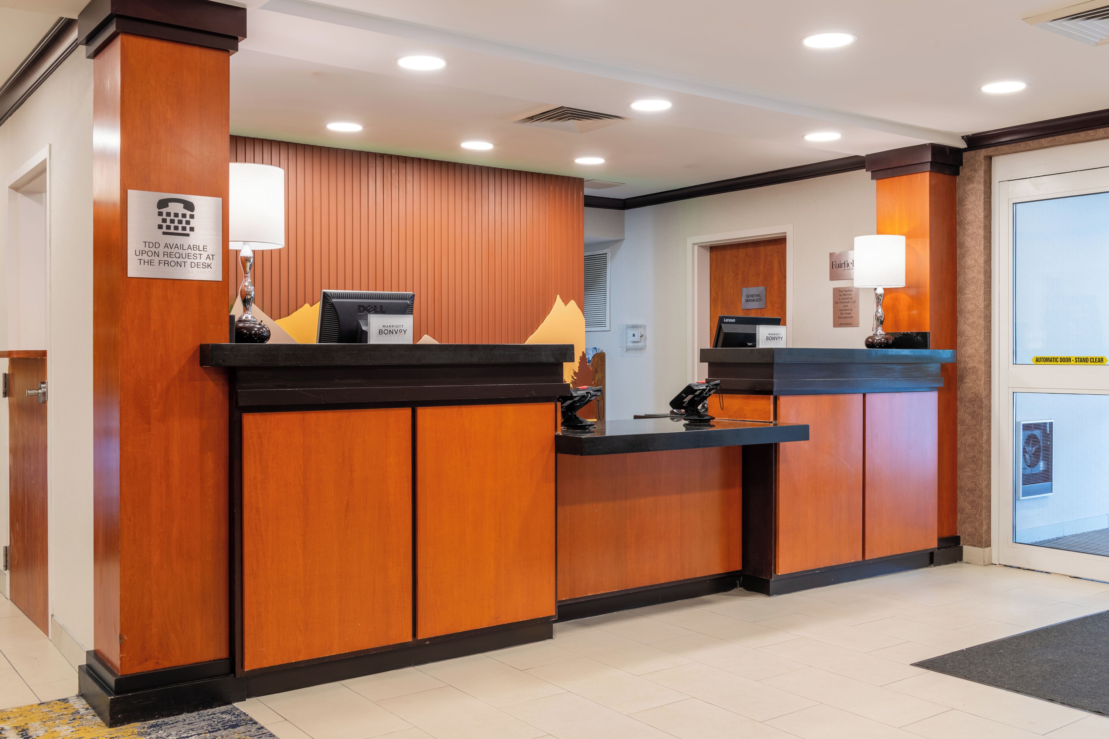 A reception desk with a wooden finish, a black counter, and a sign indicating TDD availability.