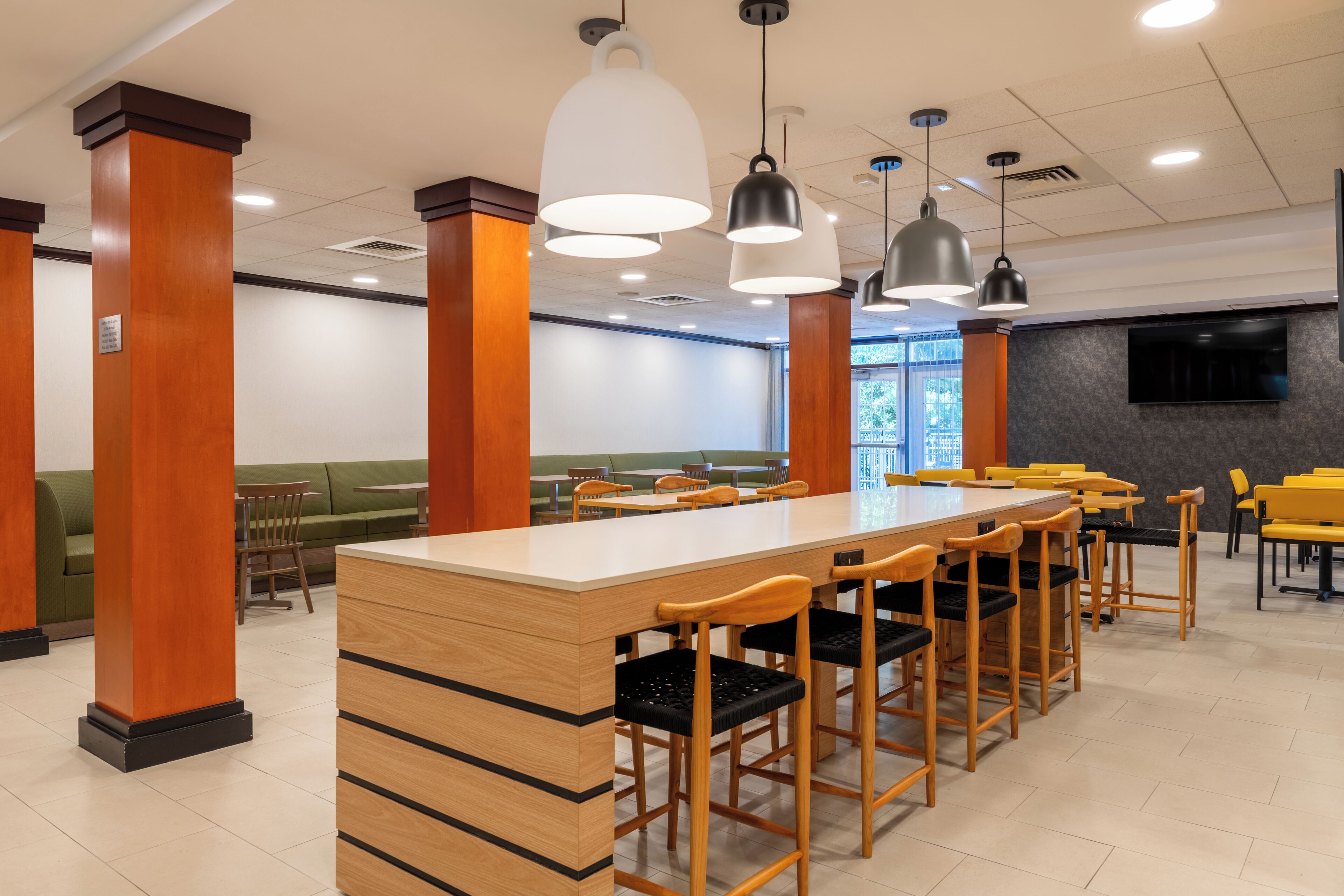 Eine geräumige Cafeteria mit hohen Holzsäulen, einem langen Tisch in der Mitte und mehreren Barhocker.