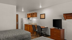 A compact room with a bed, a kitchenette, a desk with chairs, a television, and a wardrobe. - WoodSpring Suites Evansville East (Evansville)