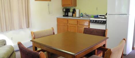 A compact kitchen with a dining table, chairs, a refrigerator, a stove, and a microwave.