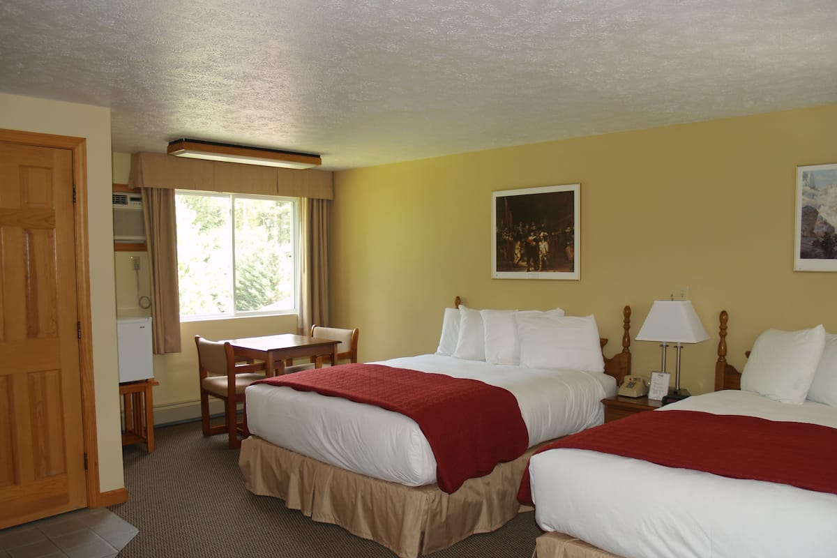 A hotel room with two beds, a desk, a chair, a window with curtains, a painting on the wall, and a door.