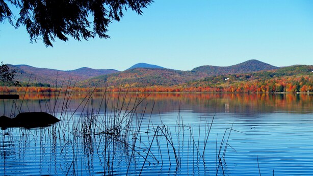 Um lago tranquilo com reflexos de árvores e montanhas ao fundo.