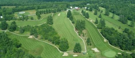 Vue aérienne d’un parcours de golf comportant plusieurs allées, des bunkers de sable et un club-house.