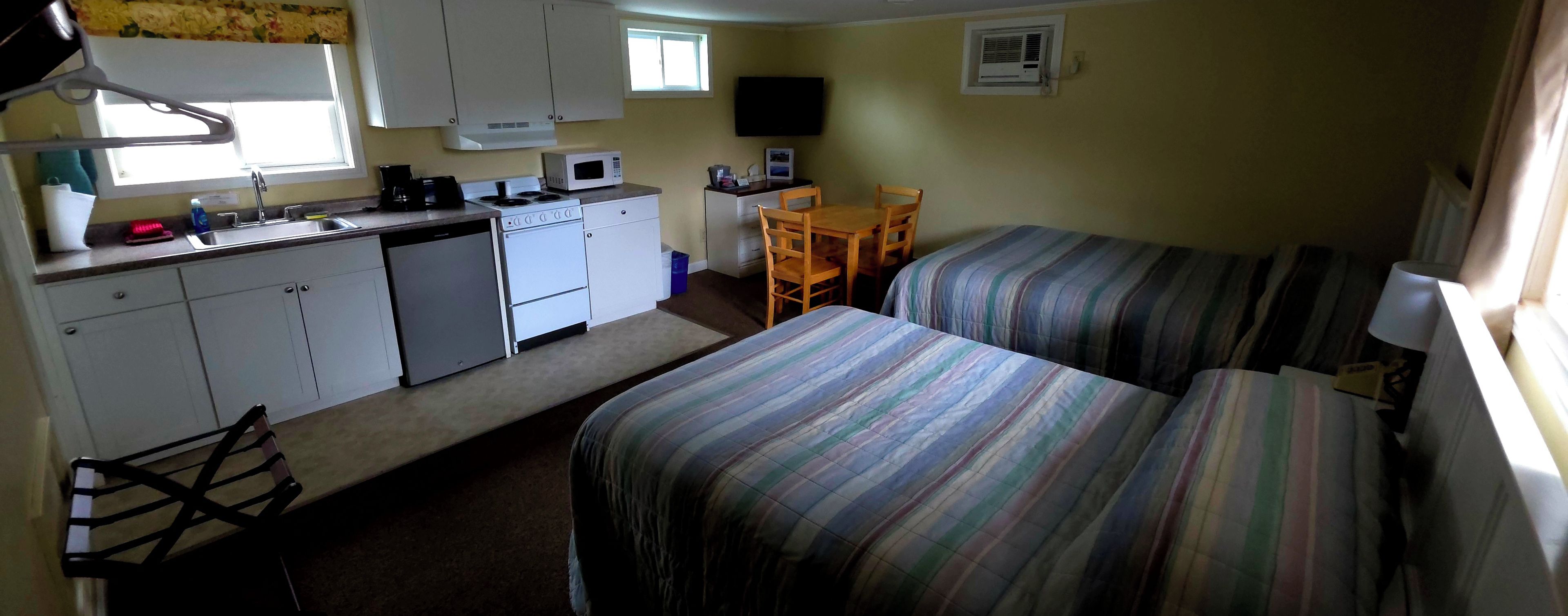 Une chambre compacte comprenant un coin cuisine, deux lits simples, une petite table et un téléviseur.
