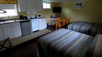 Une chambre compacte comprenant un coin cuisine, deux lits simples, une petite table et un téléviseur.