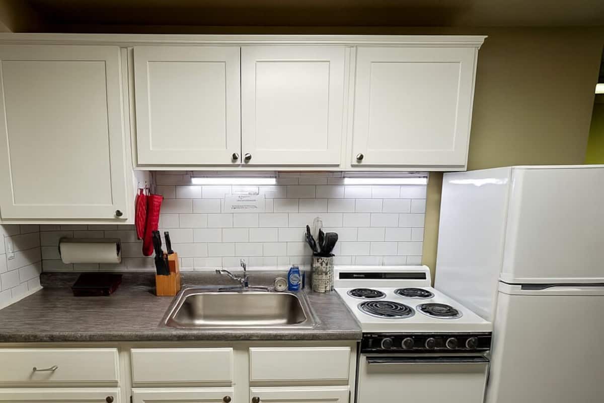 A kitchen with white cabinets, a stainless steel sink, a stove, and a refrigerator.
