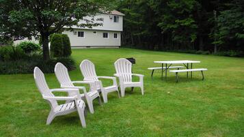 A grassy outdoor area with four Adirondack chairs and a picnic table.