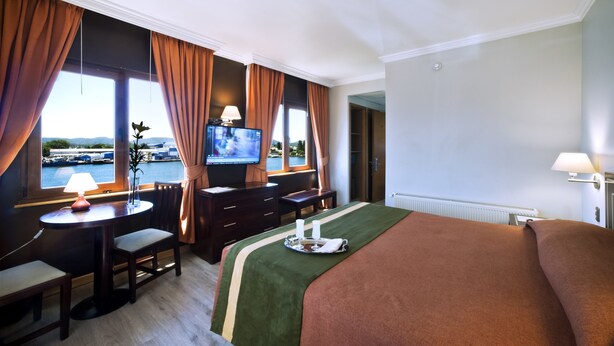 Habitación de hotel con cama, escritorio, silla, televisión y vista al mar.