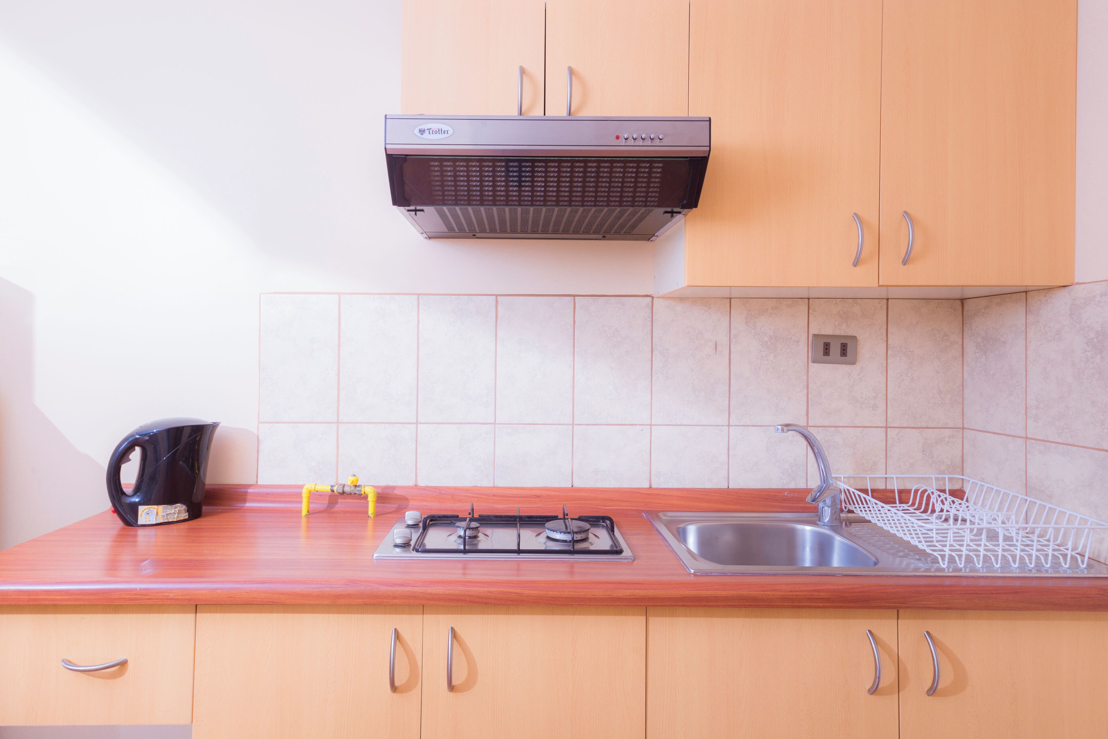 Een keuken met houten kastjes, een roestvrijstalen spoelbak, een gasfornuis en een waterkoker.