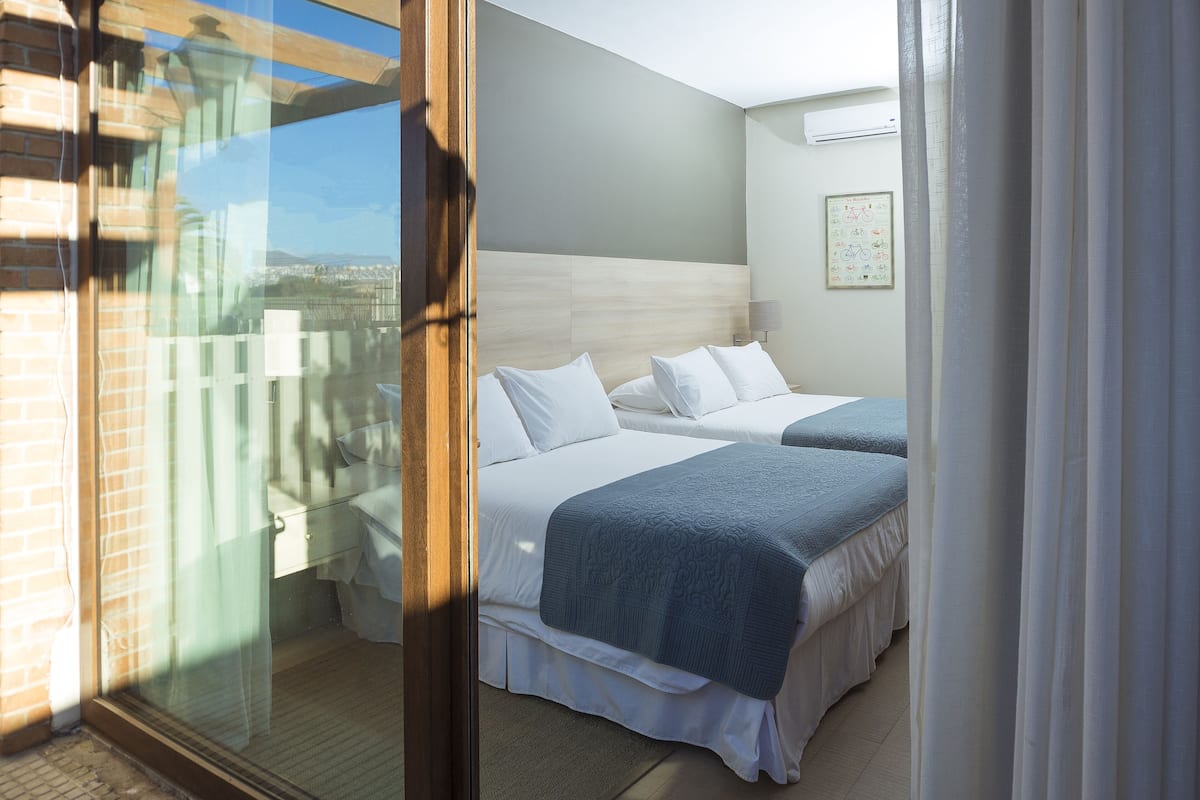 Habitación de hotel con dos camas, un ventanal grande y vistas a la ciudad.