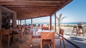 Un amplio espacio de comedor al aire libre con mesas y sillas de madera, ventanas grandes con vistas al océano y una estructura de techo de madera.