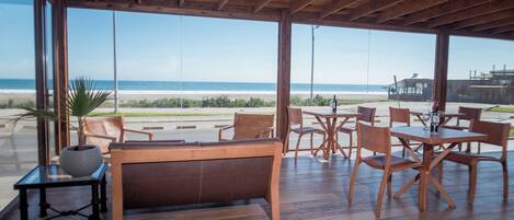 A beachside restaurant with wooden furniture and large windows overlooking the ocean.