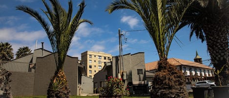 A building with a flat roof and a small tower, surrounded by palm trees and a grassy area.