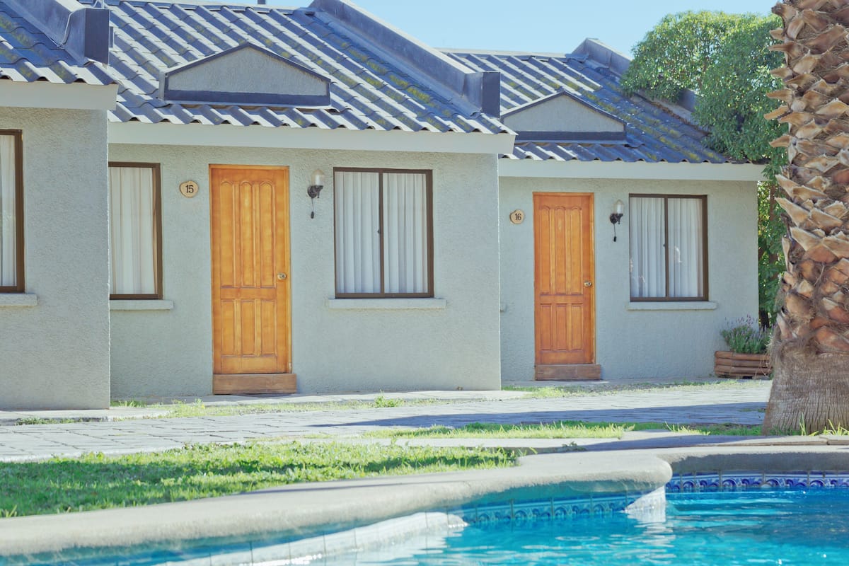 Fila de edificios de dos pisos con puertas numeradas, una piscina y una palmera.