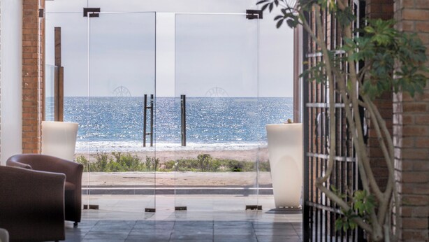 Un interior moderno con vistas al mar, que incluye una puerta de cristal, una zona de estar y una planta en maceta.