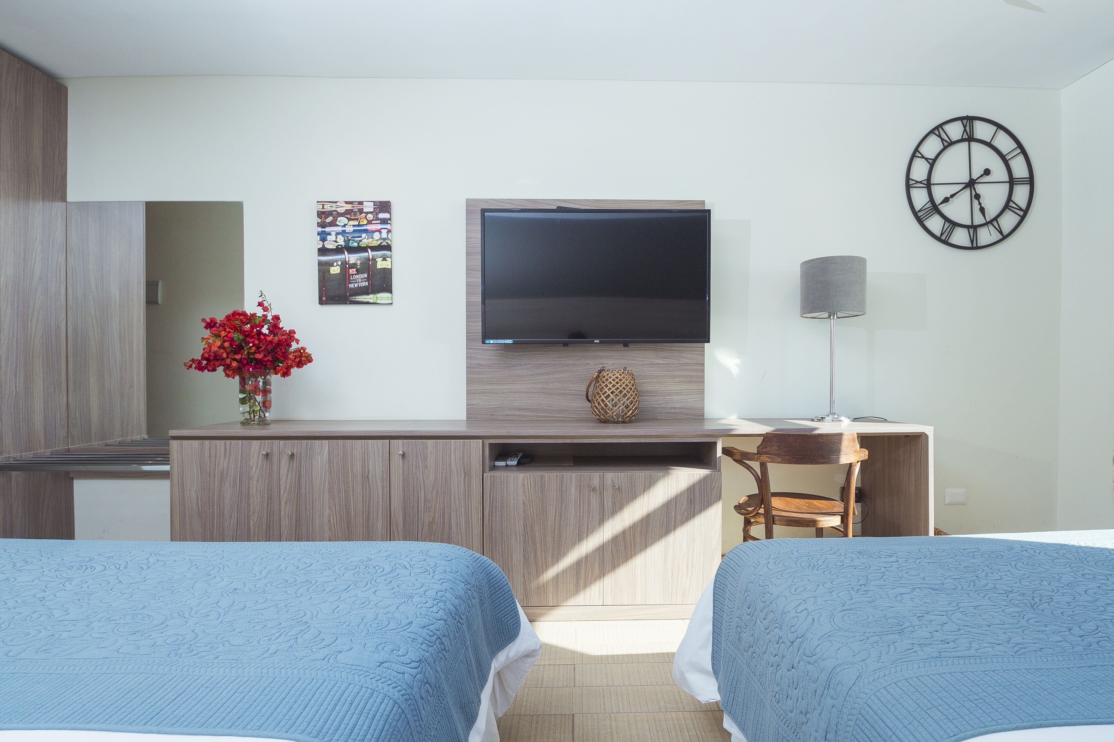 Habitación de hotel con dos camas, televisión, escritorio, lámpara y un reloj de pared.