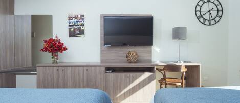 Habitación de hotel con dos camas, televisión, escritorio, lámpara y un reloj de pared.