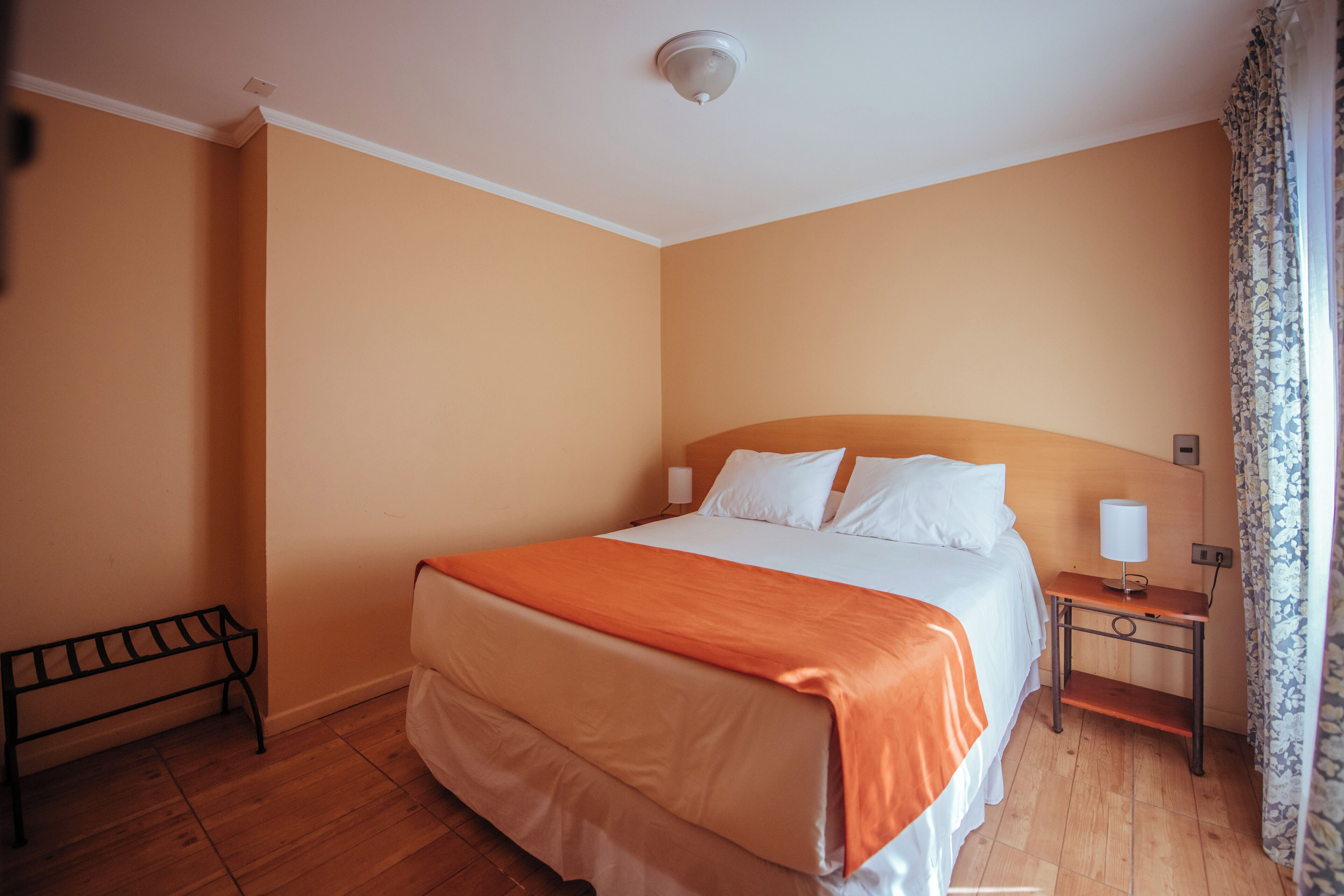 Una habitación de hotel con una cama grande, una mesita de noche con lámpara y un banco contra la pared.