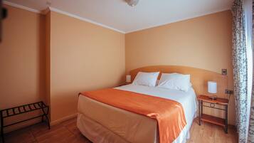 A hotel room with a large bed, a bedside table with a lamp, and a bench against the wall.