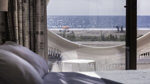 Una silla hamaca y una mesita junto a una ventana con vistas a la playa.
