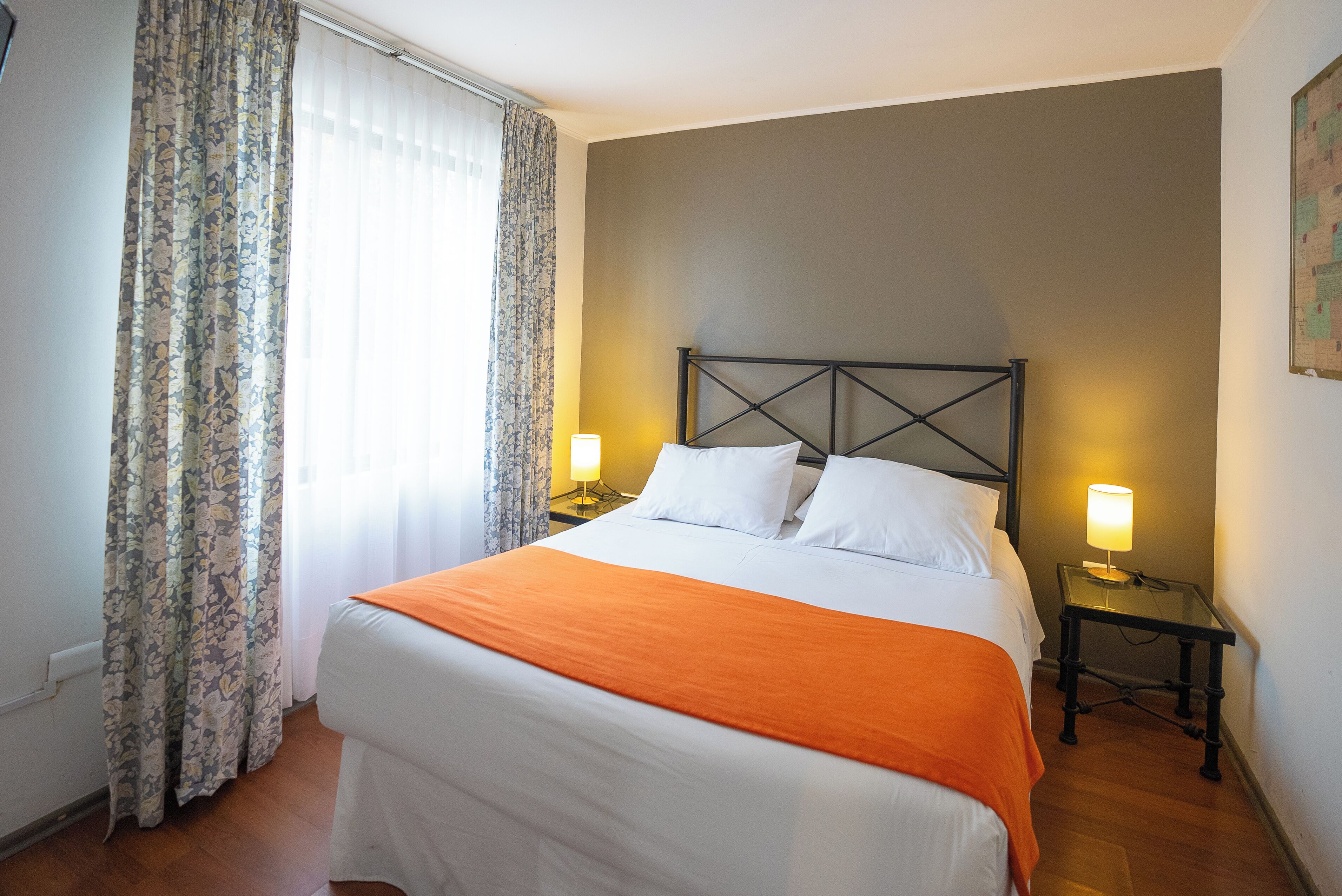 Een hotelkamer met een bed, twee bedlampen en een raam met gordijnen.