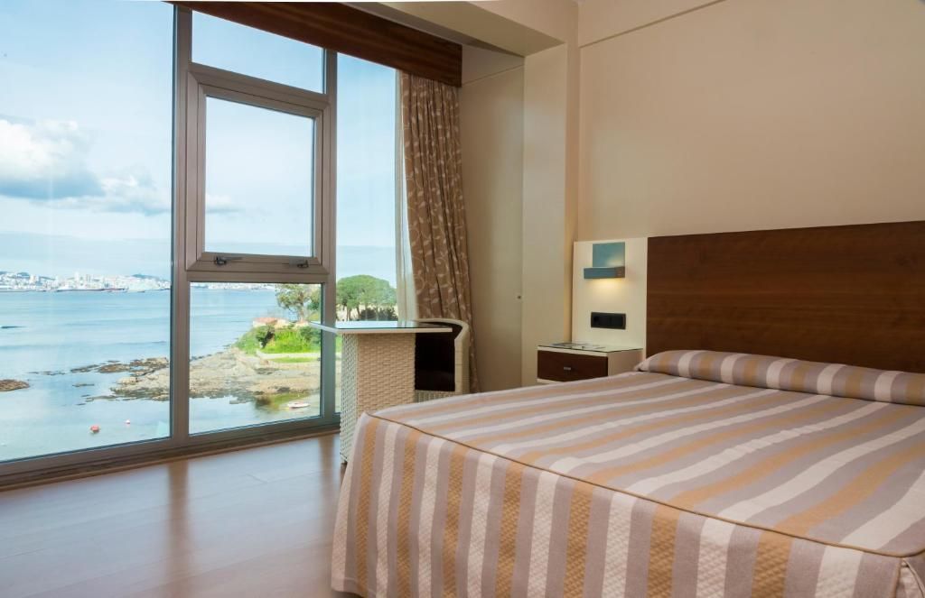 Ein Hotelzimmer mit großem Fenster und Blick auf das Meer sowie die Stadt.