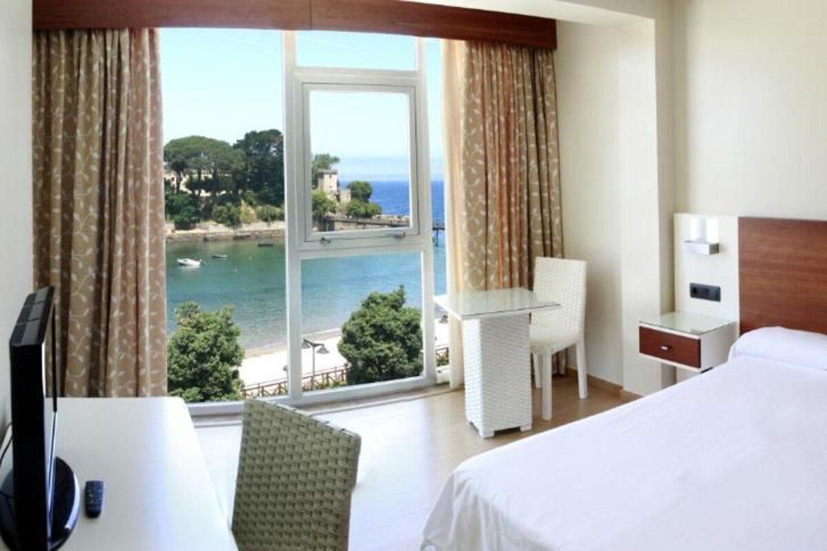 A hotel room with a large bed, a desk, a chair, and a view of the sea.