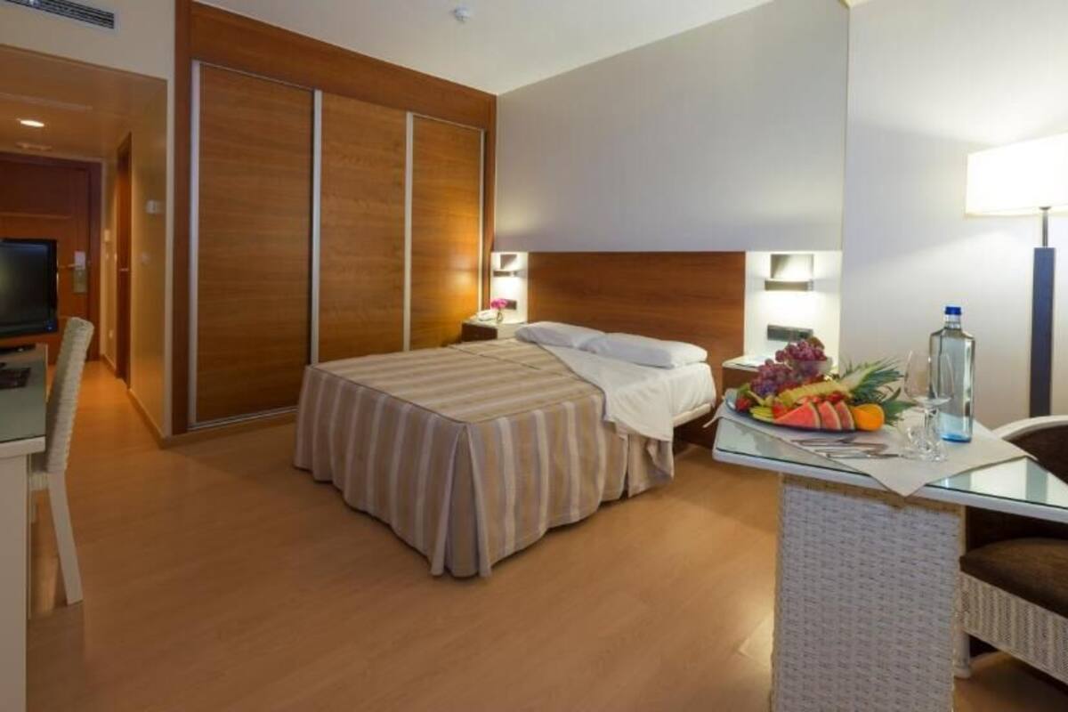 A hotel room with a bed, a desk with a laptop, a television, a wardrobe, and a fruit basket.