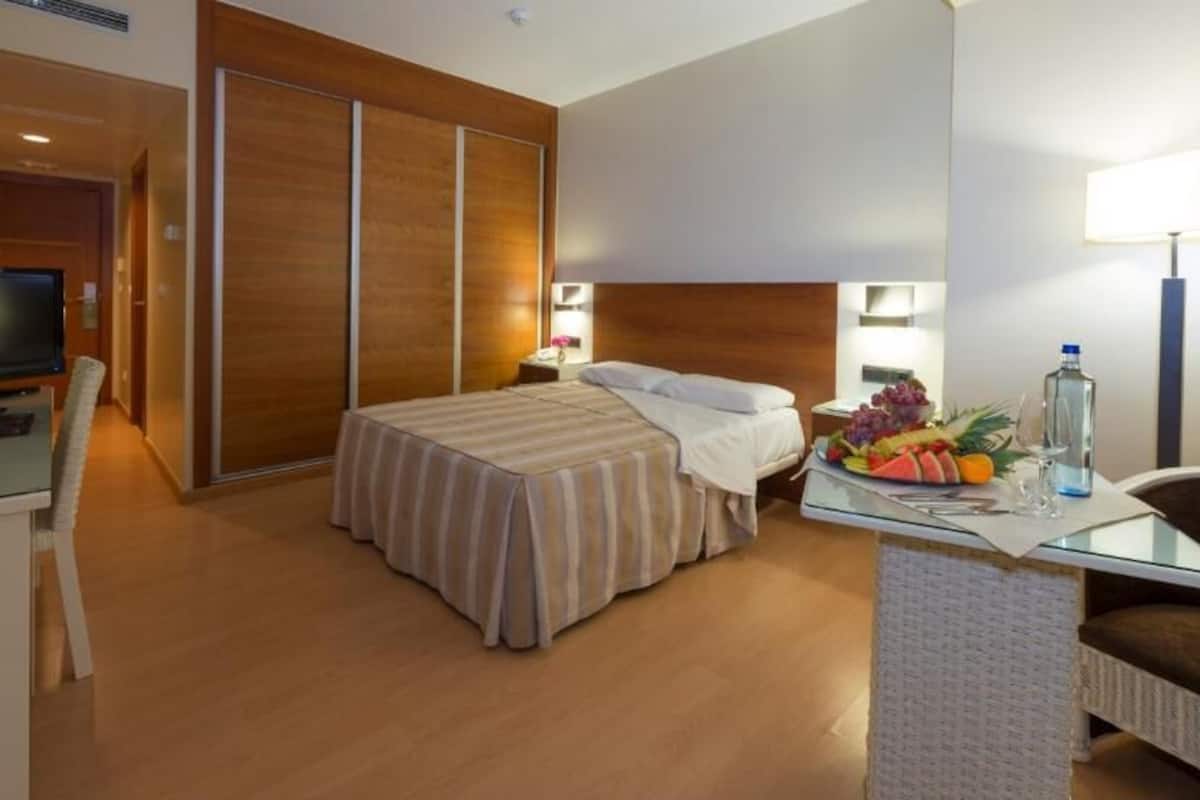 A hotel room with a bed, a desk with a lamp, a TV, and a fruit basket.