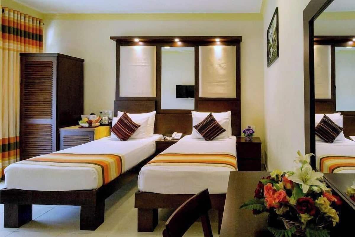 Ein Hotelzimmer mit zwei Einzelbetten, einem Holzschrank, einem Schreibtisch mit Stuhl und einem Blumenstrauß.