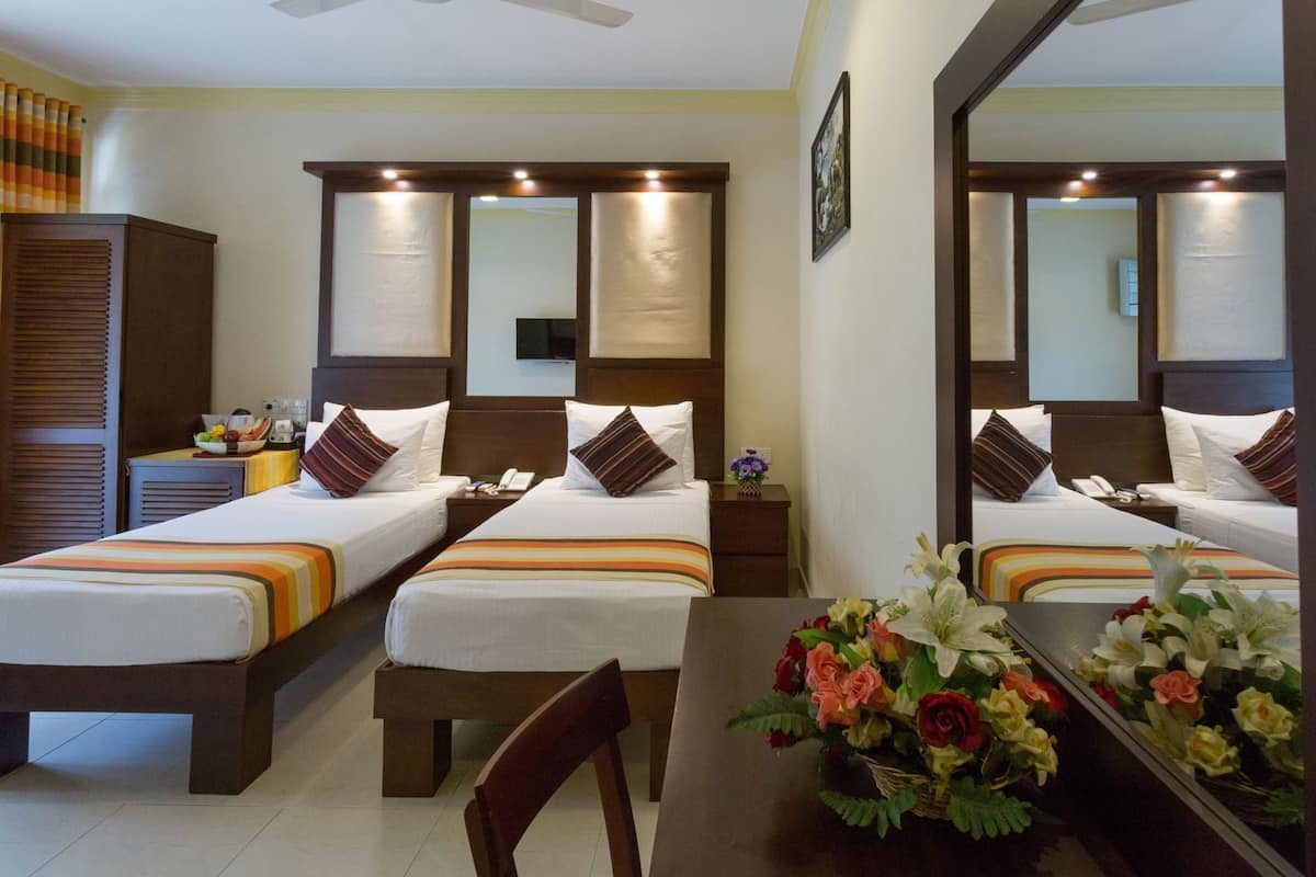 Ein Hotelzimmer mit zwei Betten, einem Schreibtisch, einem Stuhl, einem Spiegel und einer Vase mit Blumen.