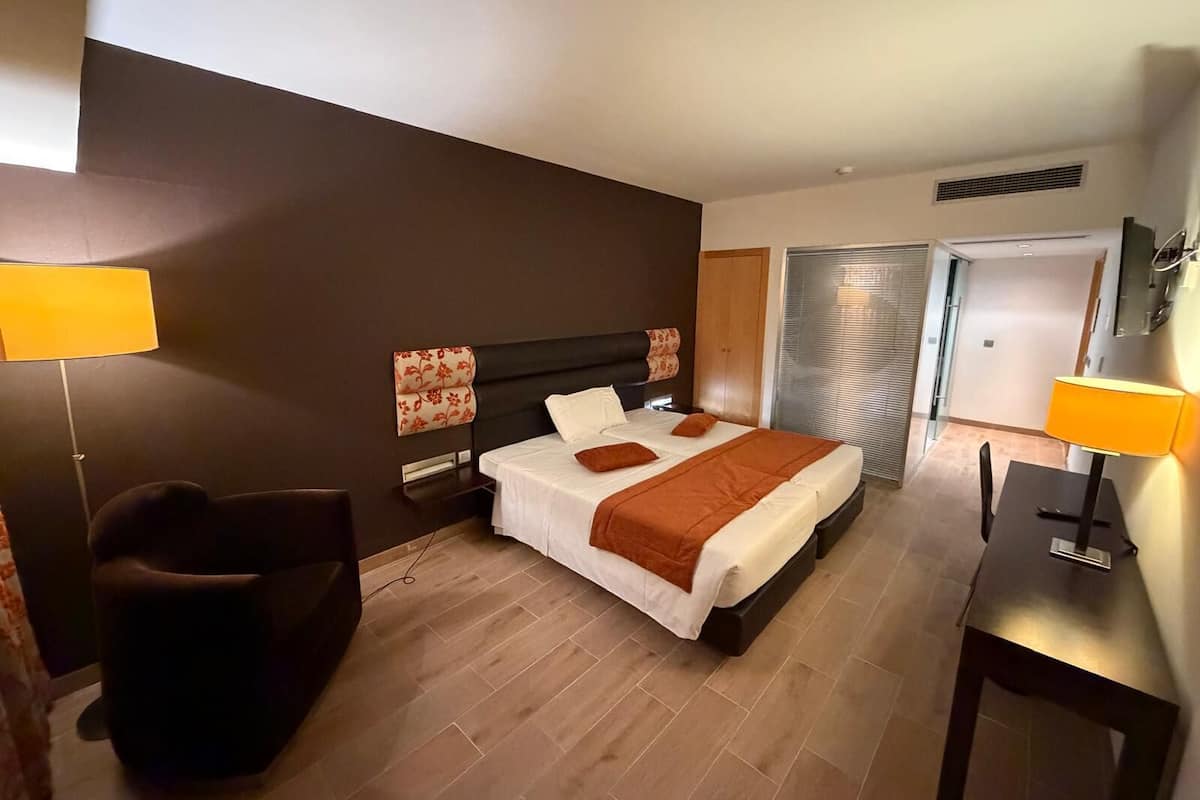 Ein Hotelzimmer mit Bett, Nachttischen, einem Sessel und einem Schreibtisch.