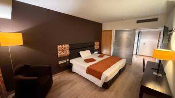 Una habitación de hotel con una cama, mesitas de noche, una silla y un escritorio.