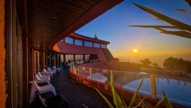 Un edificio moderno con piscina, sillones de descanso y vistas al atardecer.