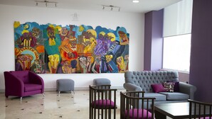 A modern interior with a colorful mural, a purple armchair, a grey sofa, and a dining table. - Hotel Lois Veracruz (Boca del Río)