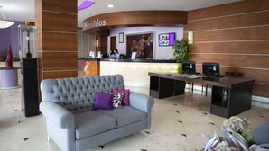 A reception area with a grey sofa, a reception desk, and a wooden wall. - Hotel Lois Veracruz (Boca del Río)