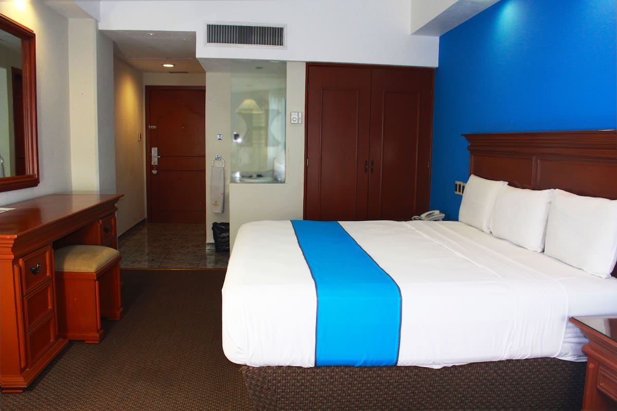 A hotel room with a large bed, a wooden desk, and a mirror.