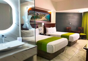 Habitación de hotel con dos camas, un baño con lavamanos, un cuadro en la pared y vistas a la ciudad.