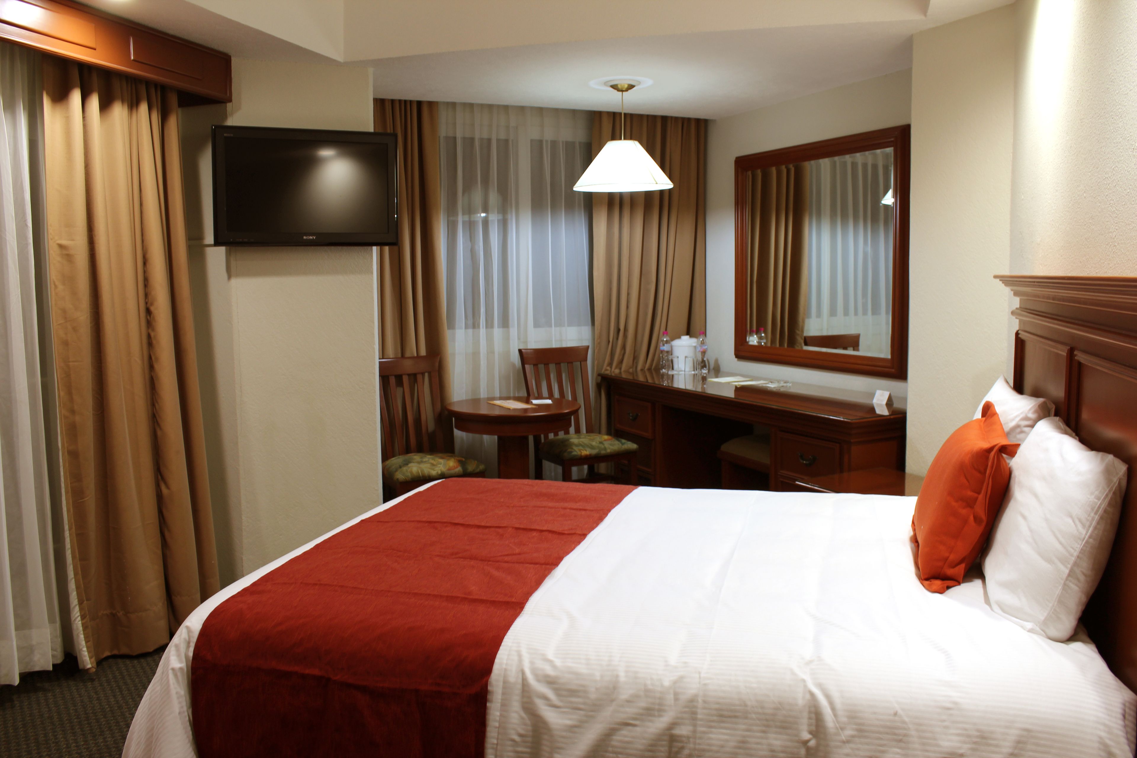 Una habitación de hotel con una cama, un escritorio, una silla, un televisor y un espejo.