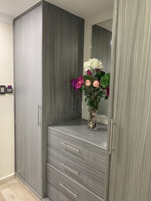 Een kast met spiegel, een vaas met bloemen en een lichtschakelaar aan de muur.