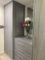 Un armario con espejo, un jarrón con flores y un interruptor de luz en la pared.