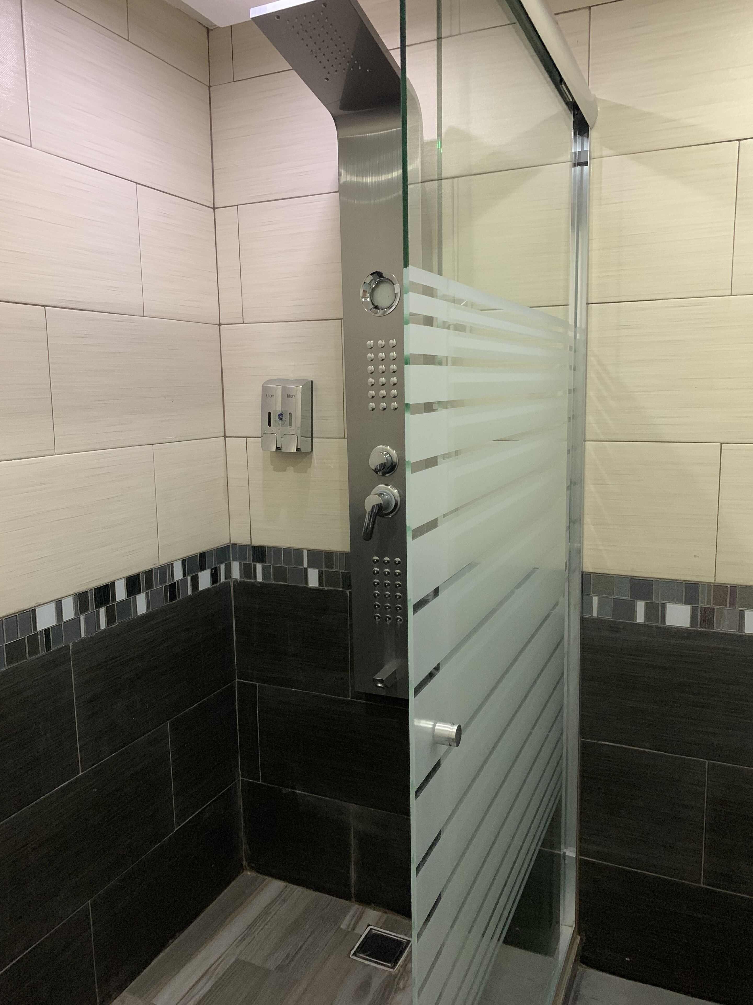 Un baño moderno con cabina de ducha de vidrio, paredes con azulejos y panel de control.