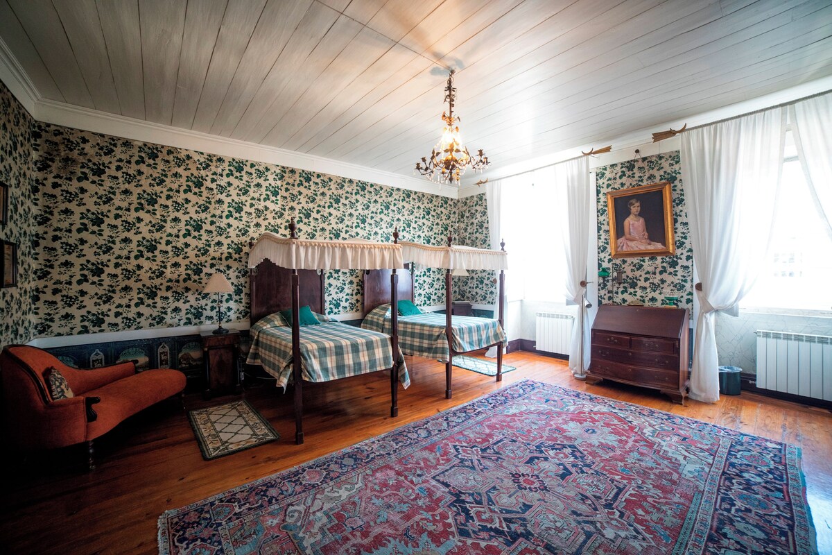 Una habitación con una cama con dosel, un aparador de madera, un sofá rojo y una alfombra estampada.