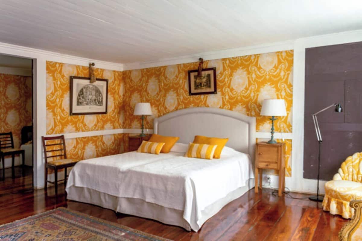 A bedroom with a large bed, two bedside tables with lamps, a chair, and a door.