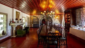 A long dining table with chairs, a chandelier, and a stone fireplace. - Casa Do Cimo (Fundao)