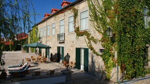 A stone building with green shutters, a courtyard with lounge chairs, and a pergola. - Casa Do Cimo (Fundao)