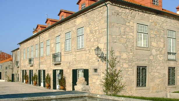 A stone building with multiple windows and balconies, a courtyard with a reflecting pool, and a street lamp. - Casa Do Cimo (Fundao)