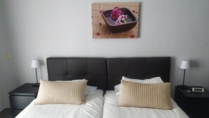 Una cama doble con dos almohadas, un cabecero oscuro y una mesita de noche con una lámpara.