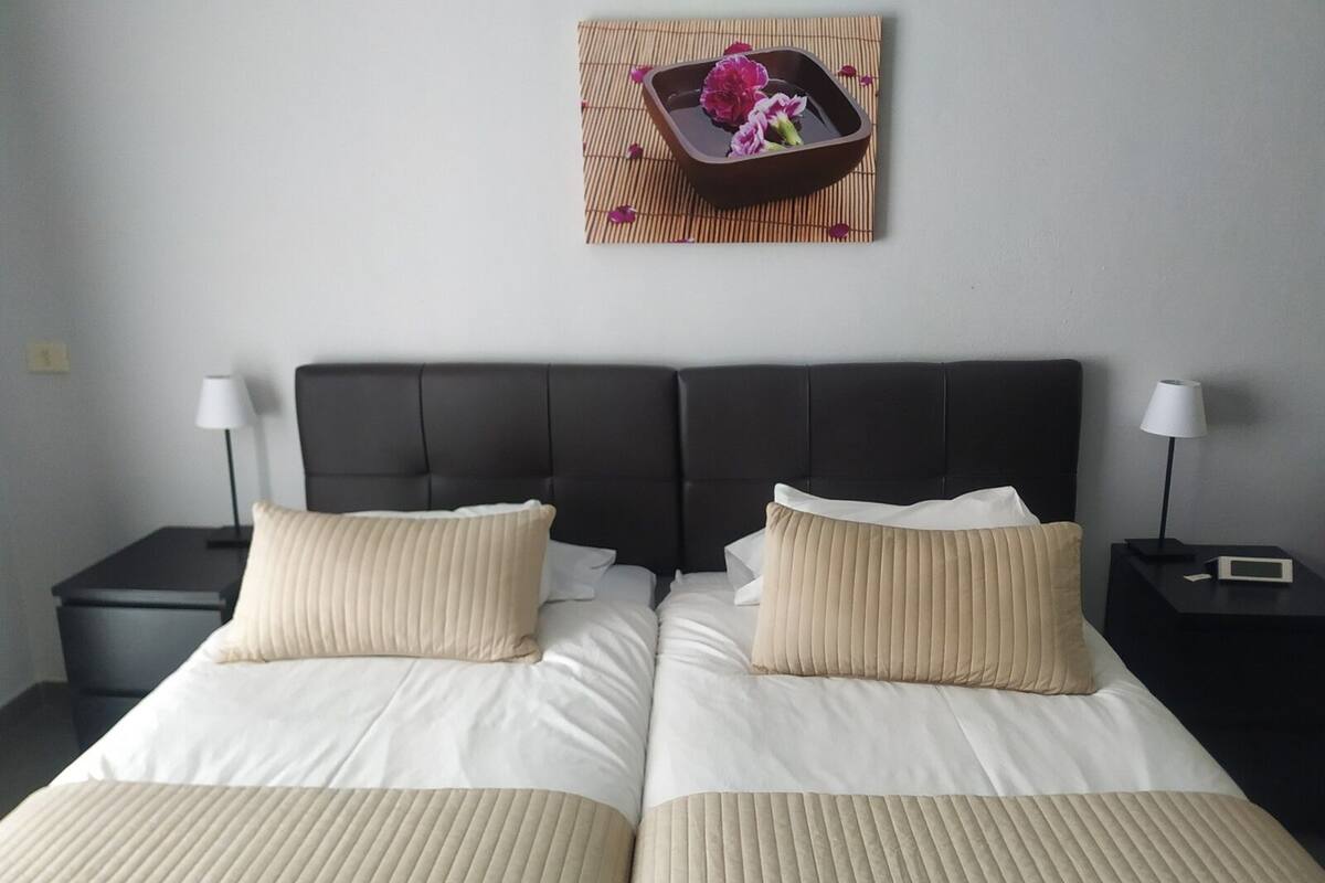 A double bed with two pillows, a dark headboard, and a bedside table with a lamp.