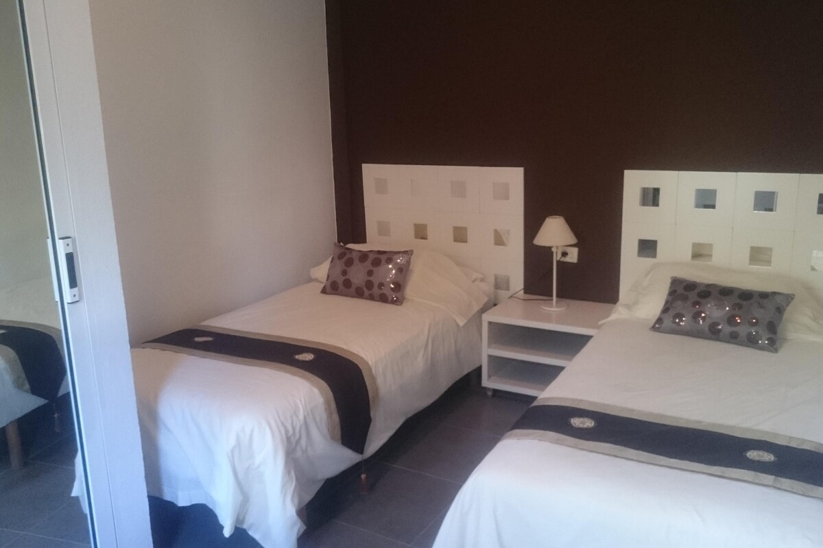 Una habitación de hotel con dos camas individuales, cada una con una almohada y una mesita de noche con lámpara.